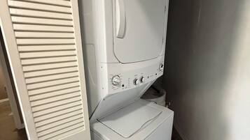 Un área de lavandería compacta con lavadora y secadora de carga frontal, una puerta blanca y una cesta de ropa.