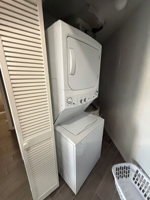 A compact laundry area with a front-loading washer and dryer, a white door, and a laundry basket. - Peaceful cozy house central location (Jacksonville)