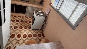 A kitchen with white cabinets, a gas stove, and a window with blinds. - Vacation Apartment 400 meters from Castanheiras Beach/Guarapari City Center (Guarapari)