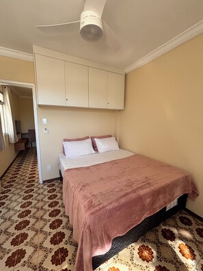 Ein Schlafzimmer mit einem Bett, einem Deckenventilator, einem Kleiderschrank und fußbodenhohen, gemusterten Fliesen.