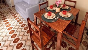 A dining area with a wooden table set for four, a grey sofa, and a ceiling fan. - Vacation Apartment 400 meters from Castanheiras Beach/Guarapari City Center (Guarapari)