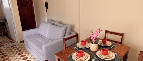 A dining area with a wooden table set for four, a grey sofa, and a ceiling fan.