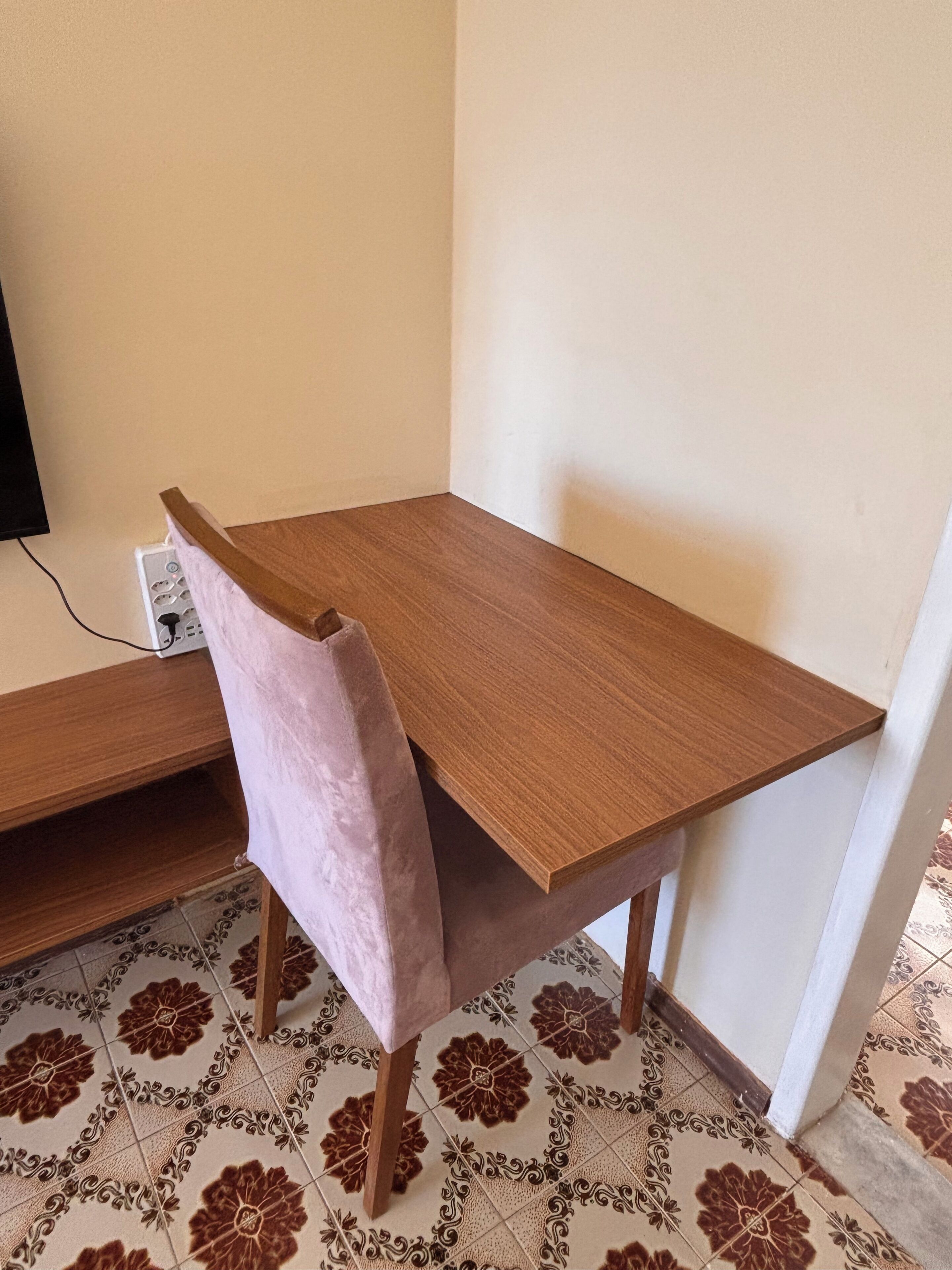 A corner of a room with a wooden table, a pink chair, and patterned floor tiles.