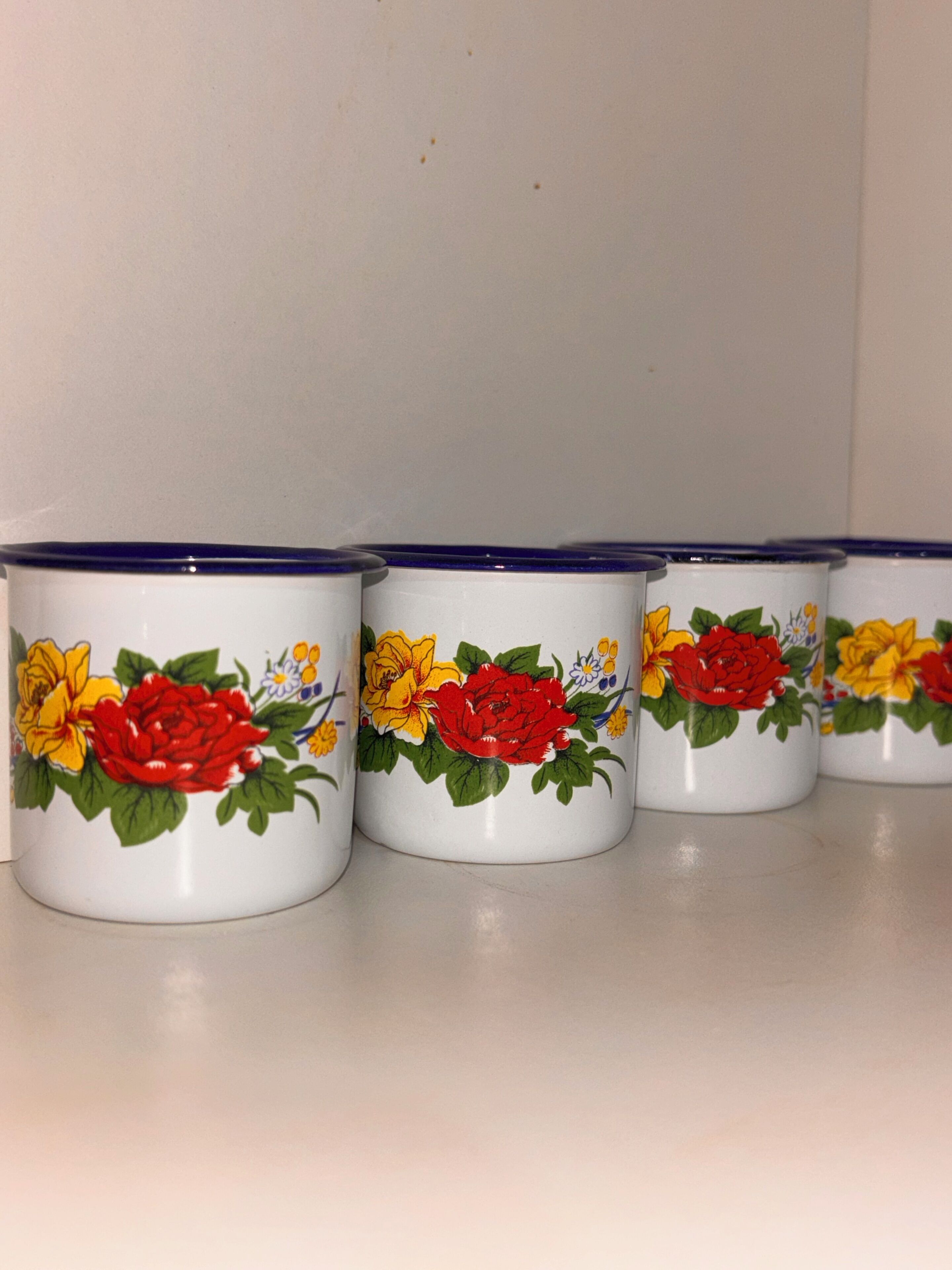Vier Keramiktassen mit floralen Mustern auf einer weißen Fläche.