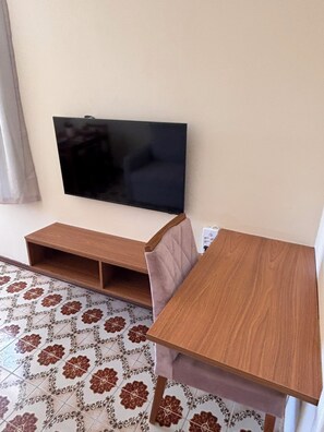 A room with a television mounted on the wall, a wooden table, and patterned floor tiles.