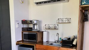 Een compacte kitchenette met een koelkast, magnetron, koffiezetapparaat en een klein spoelgedeelte.