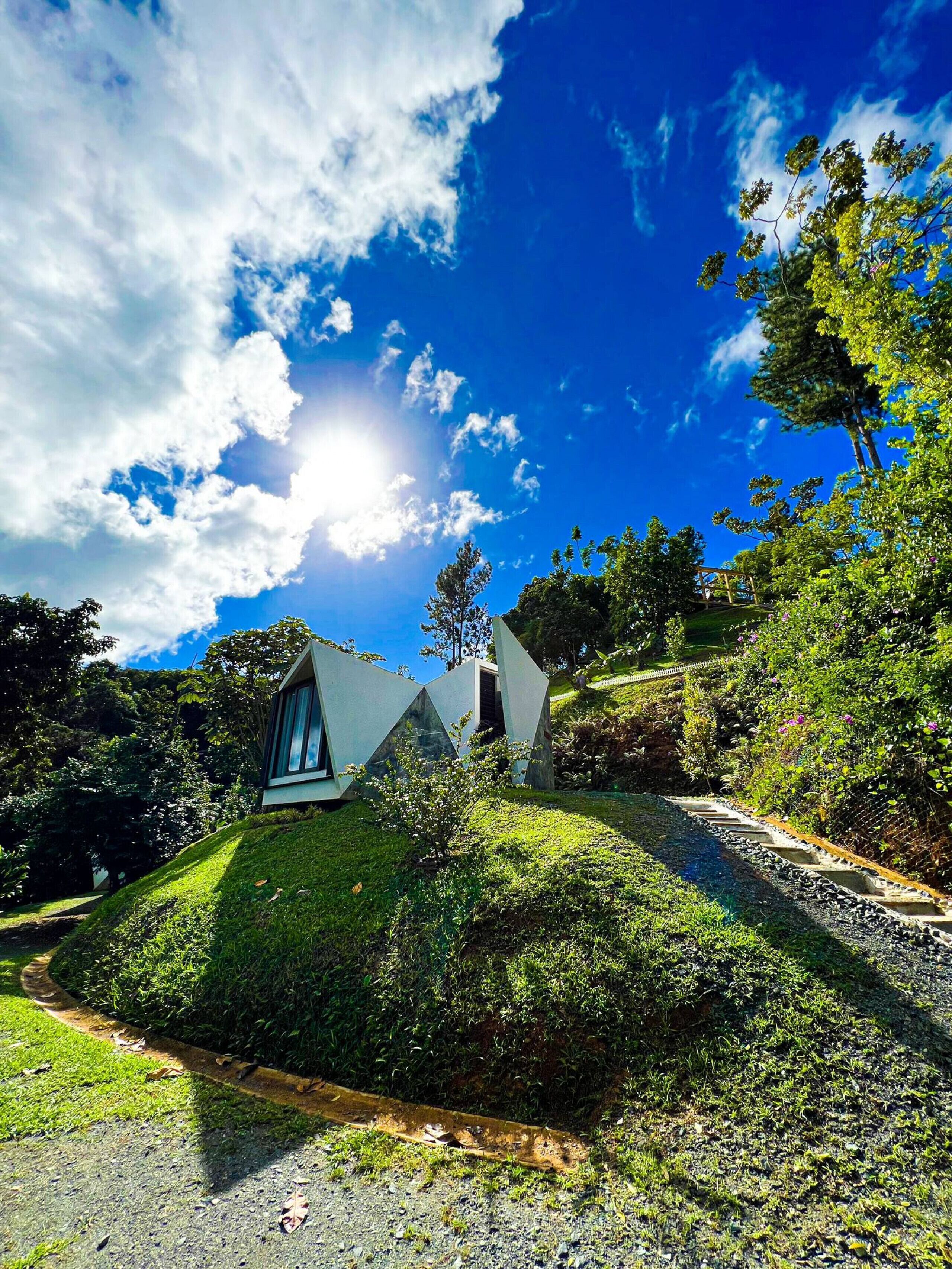 A modern house with a unique triangular design, surrounded by lush greenery and a clear blue sky.