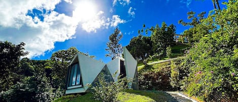 A modern house with a unique triangular design, surrounded by lush greenery and a clear blue sky.