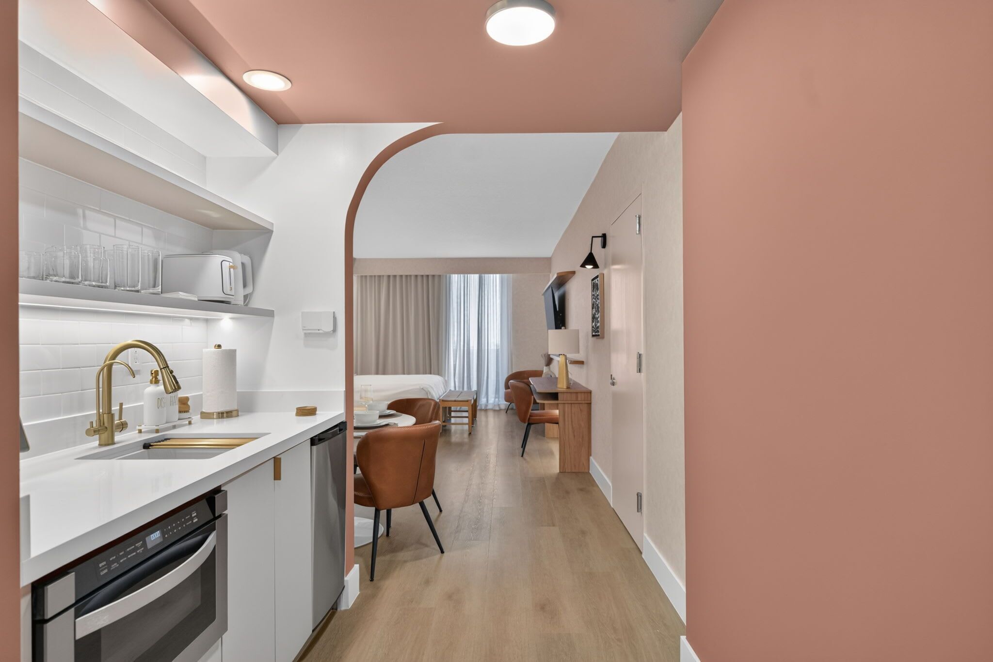 Une cuisine moderne avec des meubles blancs, un four encastré et un évier doté d’un robinet doré.