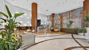 Eine großzügige Lobby mit einer zentralen Sitzecke, einer Bar und einem dekorativen Raumteiler mit geometrischen Mustern.