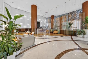 Eine großzügige Lobby mit einer zentralen Sitzecke, einer Bar und einem dekorativen Raumteiler mit geometrischen Mustern.