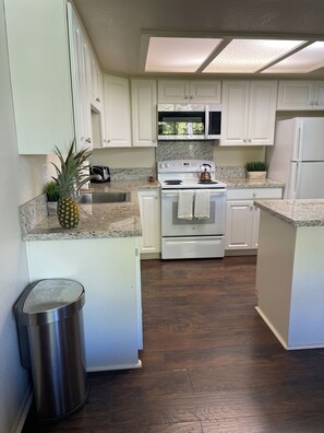 A kitchen with white cabinets, a stainless steel trash can, a microwave, and a stove. - Hallelujah Condo near Hanalei - 2 Bed 2 Bath (Princeville)