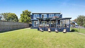 Ein zweistöckiges Haus mit überdachter Terrasse und umzäunter Garten.