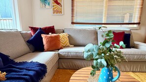 Ein Wohnzimmer mit Ecksofa, Couchtisch und einem Fenster mit Jalousien.