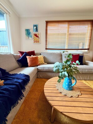 Ein Wohnzimmer mit Ecksofa, Couchtisch und einem Fenster mit Jalousien.