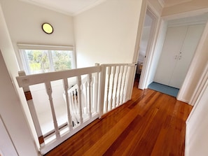 Un plancher en bois avec une rambarde blanche, une fenêtre donnant sur un paysage verdoyant et une porte blanche en arrière-plan.