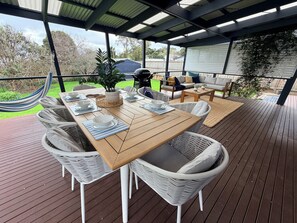 Eine Terrasse im Freien mit einem Holztisch, gedeckt für das Essen, umgeben von Korbstühlen, einer gepolsterten Couch und einer Hängematte.