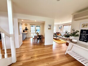 Ein geräumiger Wohnbereich mit Holzboden, einem Esstisch und einer Couch. Eine Treppe führt zu einer weiteren Ebene.