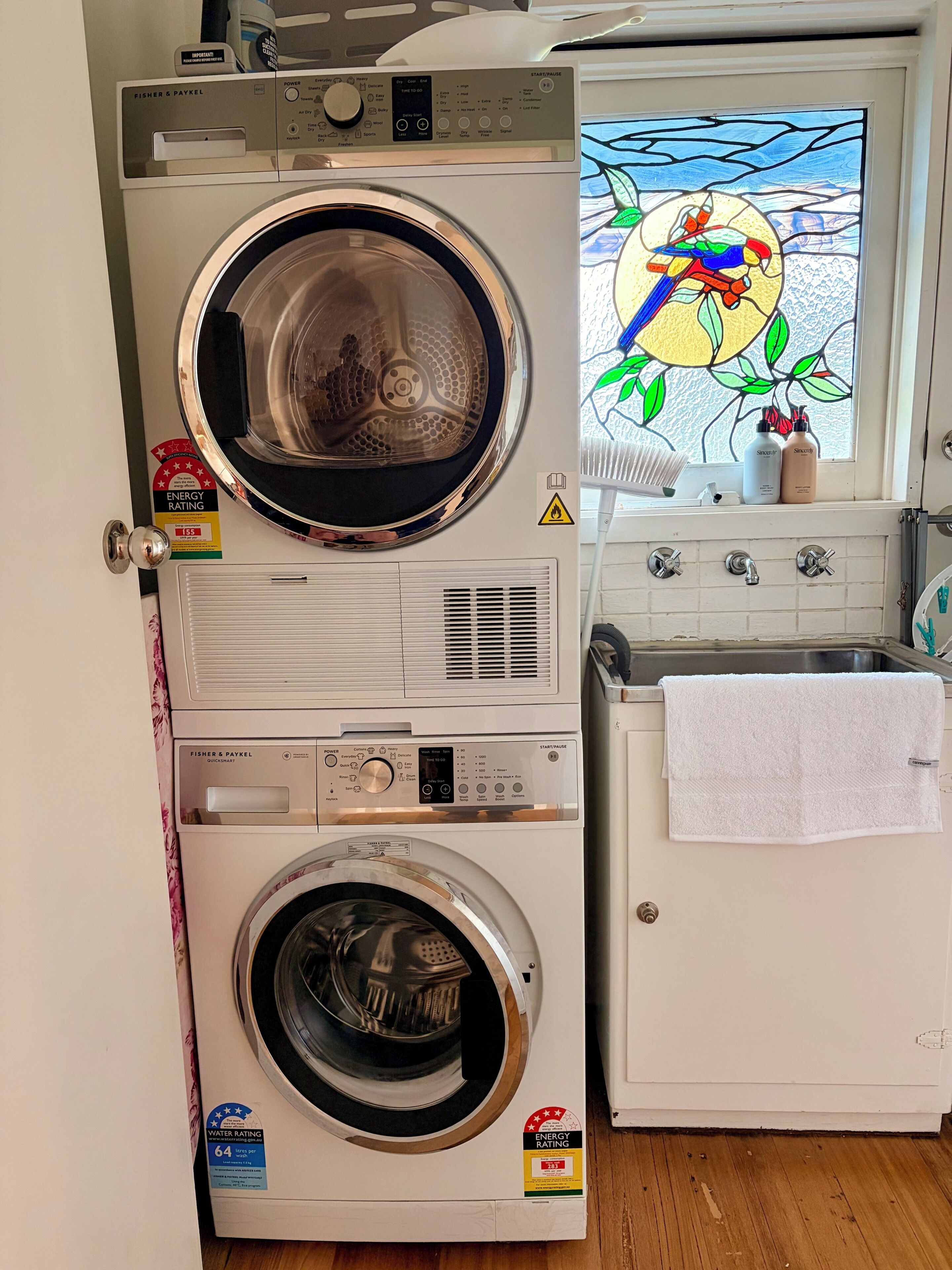 Une buanderie équipée de deux machines à laver à chargement frontal, d’un sèche-linge et d’une fenêtre ornée de vitraux.