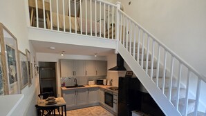 A spacious living area with a high ceiling, a staircase, a kitchen with modern appliances, and a dining area.