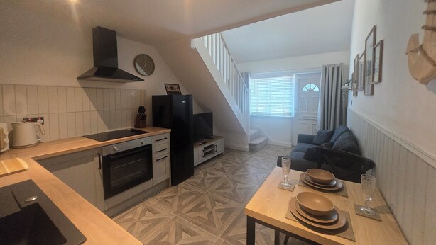 A compact kitchen with a stove, oven, and modern appliances, leading to a dining area with a table set for two.