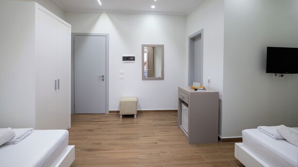 A modern hotel room with a bed, a small desk, a mirror, and a television on the wall.