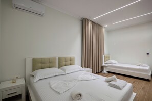 Une chambre d’hôtel avec un lit, des tables de chevet, une petite table, une lampe et une fenêtre avec des rideaux.