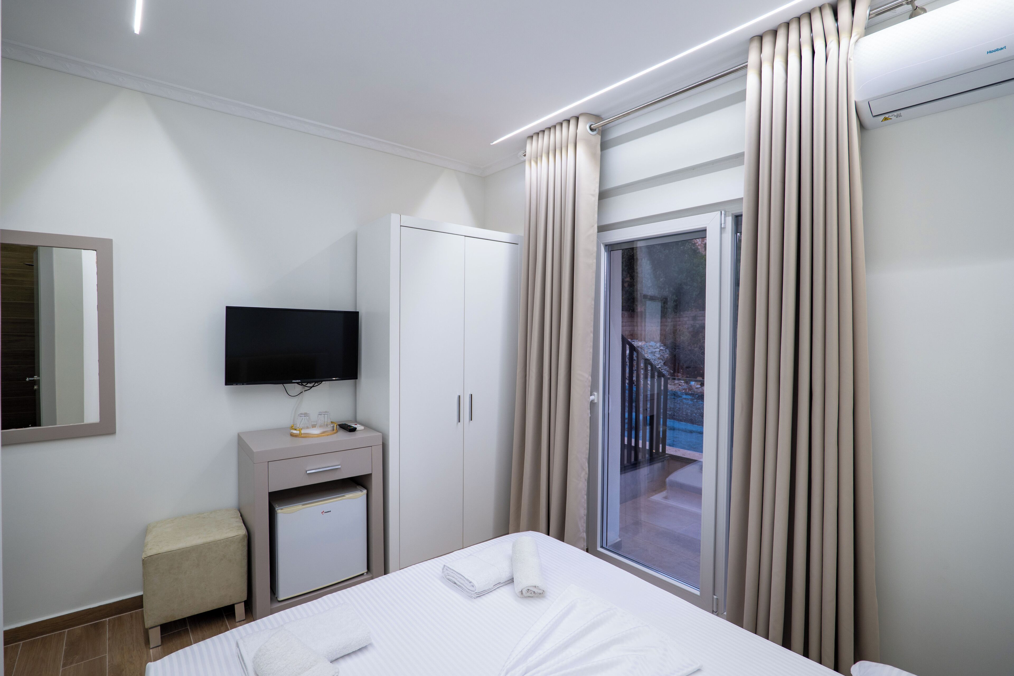 Ein Hotelzimmer mit Bett, Fernseher, Minibar, Kleiderschrank und einer Schiebetür zum Balkon.