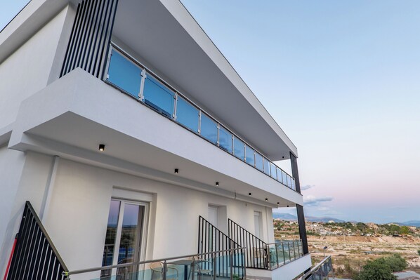 A modern two-story building with a glass balcony, a staircase, and a view of the surrounding landscape. - SulMare Rooms (Sarandë)