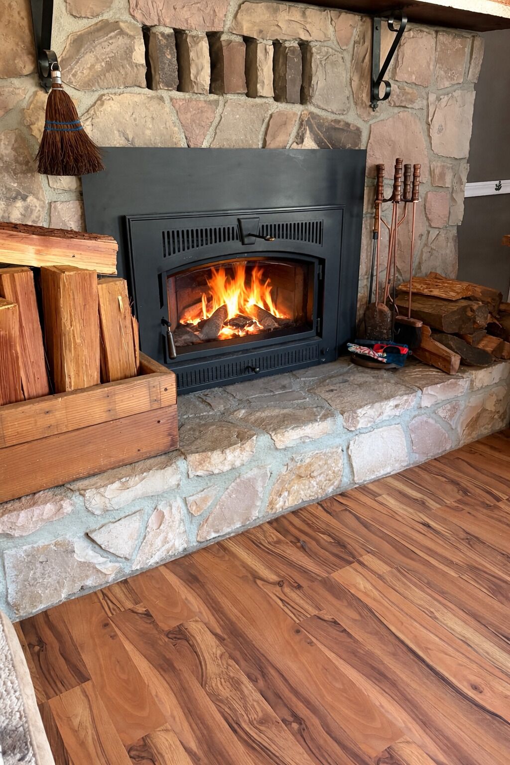 A fireplace with a stone surround, logs, and a hanging broom.