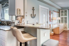 Una cocina moderna con una isla central, taburetes de bar, horno empotrado y un amplio ventanal.