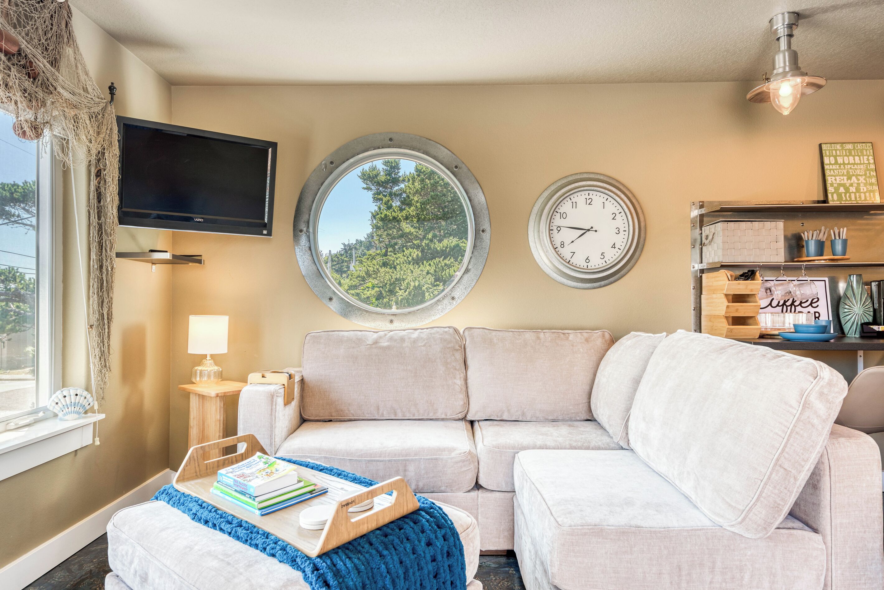 A cozy living room with a sofa, a round window, a flat-screen TV, and a wall clock.