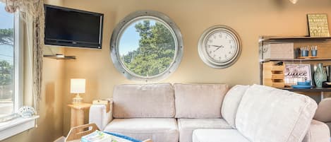 A cozy living room with a sofa, a round window, a flat-screen TV, and a wall clock.