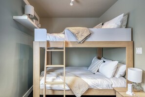 Ein Stockbett mit einer Leiter, ein Nachttisch mit einer Lampe und ein Regal über dem Bett.