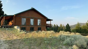 Une cabane en rondins dotée d’une véranda, d’un balcon et offrant une vue sur la forêt environnante.
