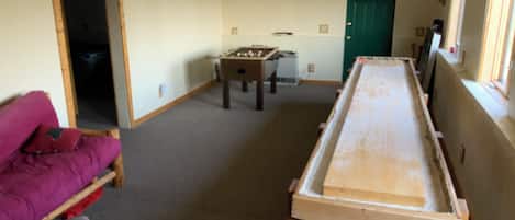 A room with a foosball table, a sofa, and a long table.