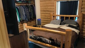Une chambre dans une cabane en bois, avec un lit superposé, un placard avec des vêtements suspendus et une fenêtre avec des rideaux.