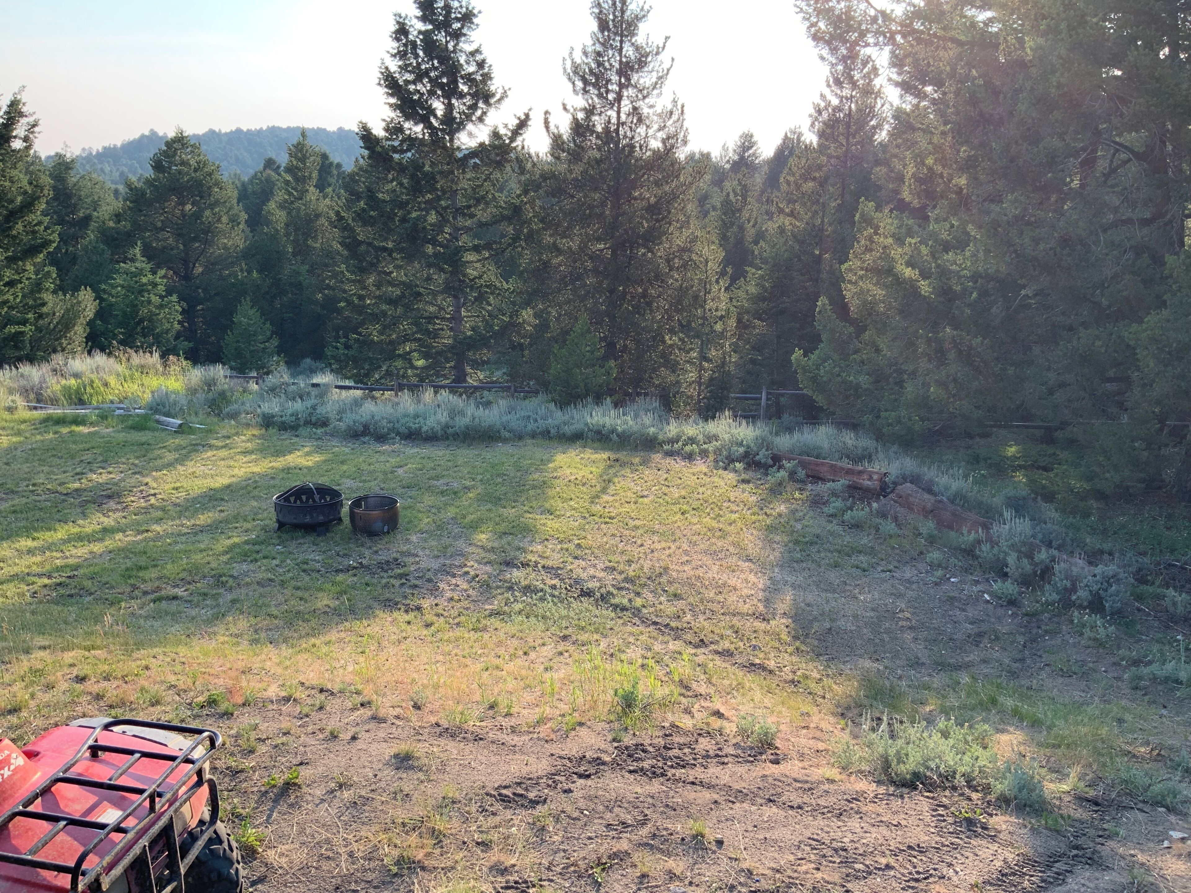 A field with a red vehicle, two metal containers, and a wooden fence.