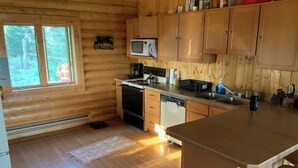 A wooden cabin kitchen with a microwave, stove, sink, and wooden cabinets.