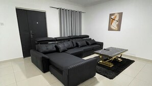 A modern living room with a sectional sofa, a coffee table, and a wall-mounted artwork. - Charming 3-bedroom apartment with AC in Accra Oyarifa (Accra Oyarifa)
