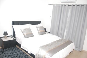 Ein Hotelzimmer mit Bett, Nachttisch, Lampe und einem fenster mit Vorhängen.