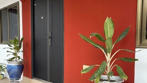 A building with a red exterior, a black door, and two large blue planters with green plants on a tiled floor. - Charming 3-bedroom apartment with AC in Accra Oyarifa (Accra Oyarifa)