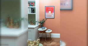 Ein Zimmer mit einem Bücherregal, einer gerahmten Werbung für Chanel-Parfüm und einem kleinen Tisch mit zwei Schalen.