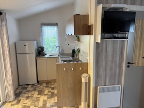 Eine kleine Küche mit Kühlschrank, Kaffeemaschine, Spüle und Fernseher.