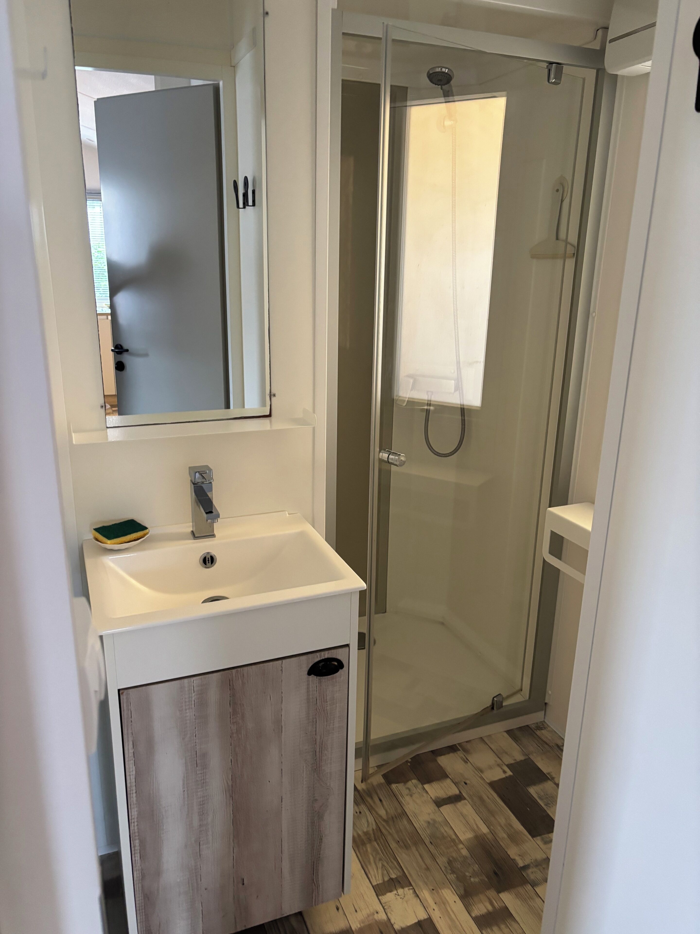 A bathroom with a white sink, a mirror, a glass-enclosed shower, and a wooden cabinet.