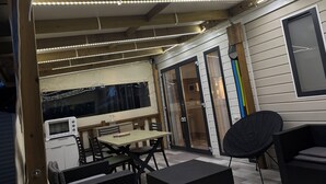 Ulkoterassi, jossa on pöytä ja tuoleja, mikroaaltouuni ja musta tuoli.