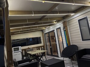 Ein Außenbereich mit Terrasse, Tisch, Stühlen, einer Mikrowelle und einem schwarzen Stuhl.