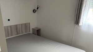Pieni huone, jossa on sänky, pieni yöpöytä, seinälle kiinnitetty kello ja ikkuna, jossa on verhot.
