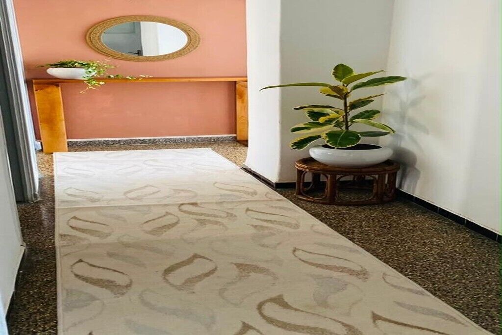 A hallway with a patterned carpet, a round mirror on the wall, a wooden bench, and a potted plant.