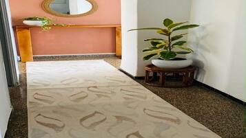 A hallway with a patterned carpet, a round mirror on the wall, a wooden bench, and a potted plant.